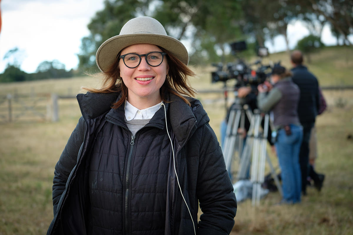 Director Lucy Gaffy is standing in the middle of a field. A camera crew is out of focus behind her.