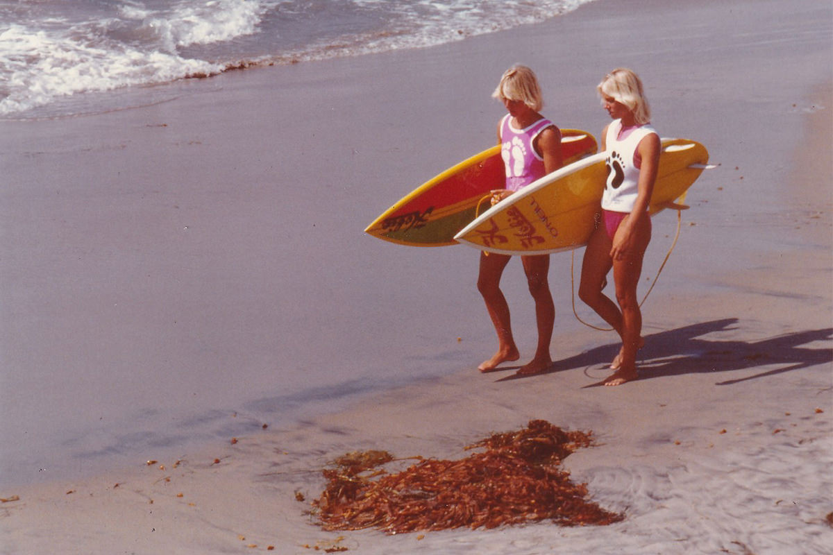 Two women, holding surfboards, walking along a beach.