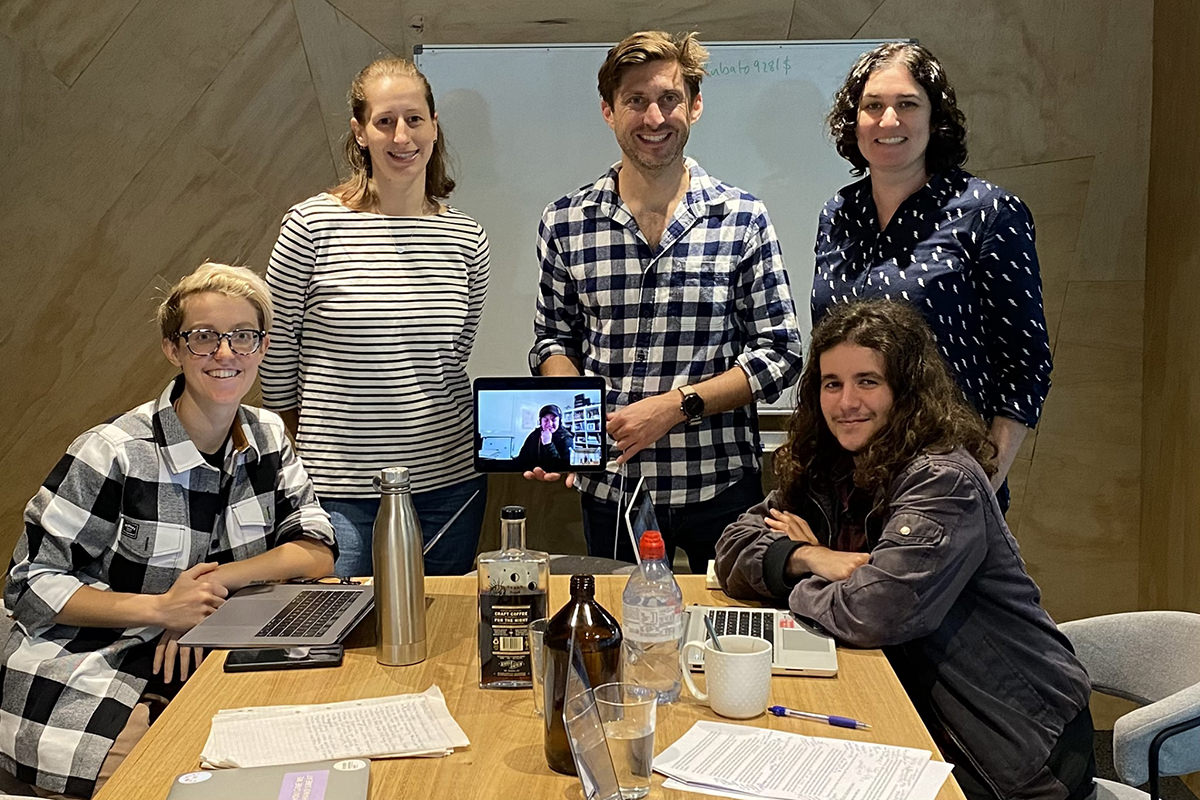 A group of people sit around a desk in a writers' room.