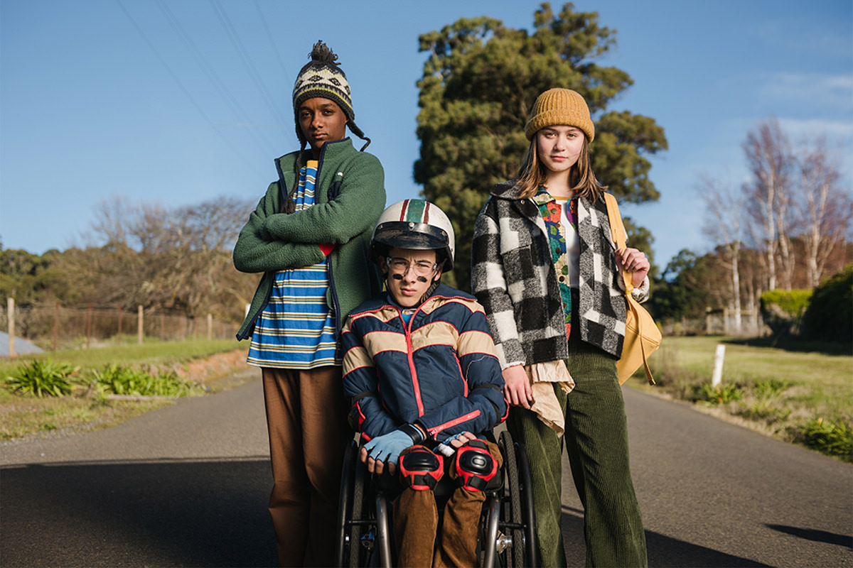 Three children huddle together on the road, one is in a wheelchair