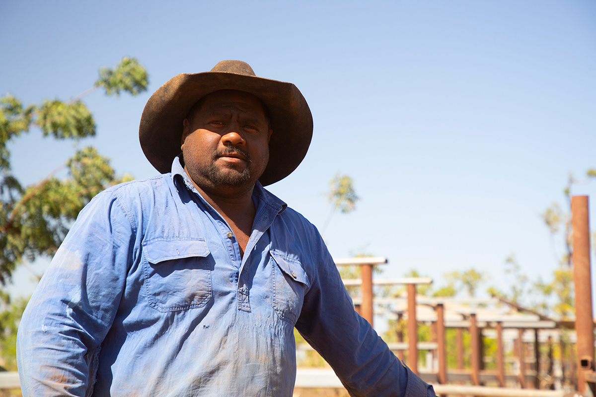 A man standing against a fence in the Outback.