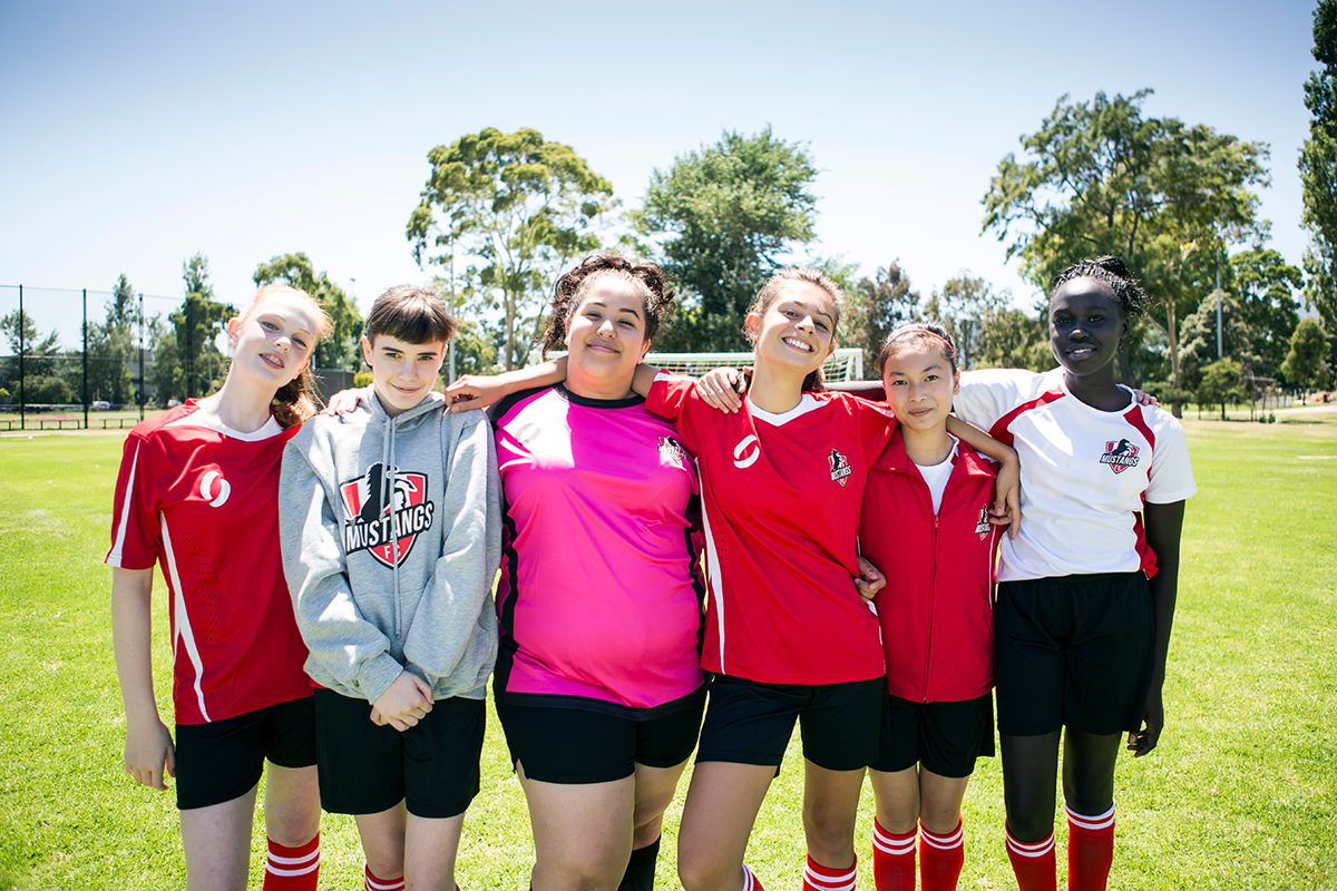 A group of young girls wearing soccer uniforms have their arms around one another