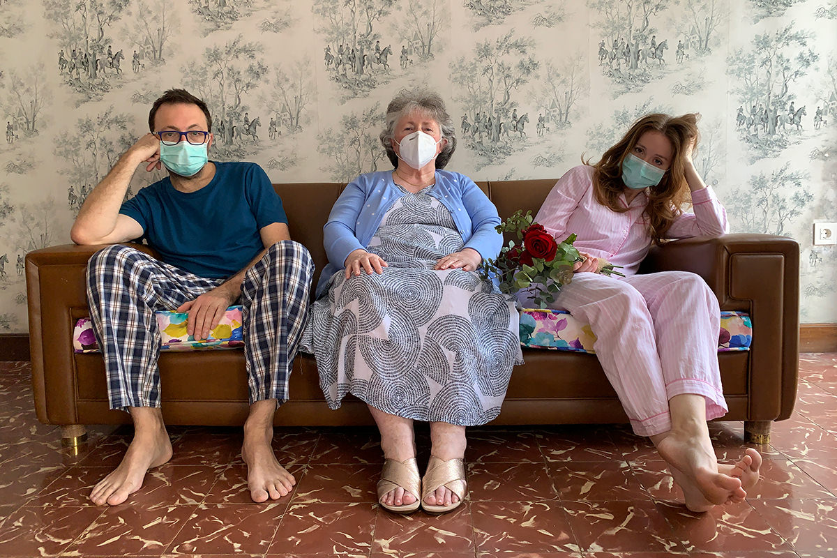Three people sit together on a couch. They are all wearing face masks.