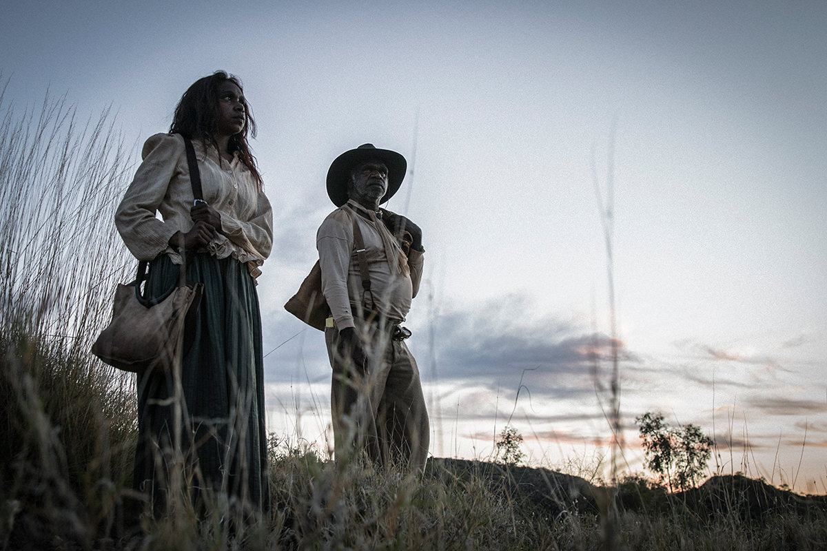 A man and a woman stand on a hilltop, looking out into the distance