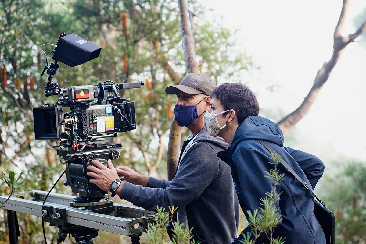 Geoff Owen and Meg White stand behind a camera on the set of Preppers