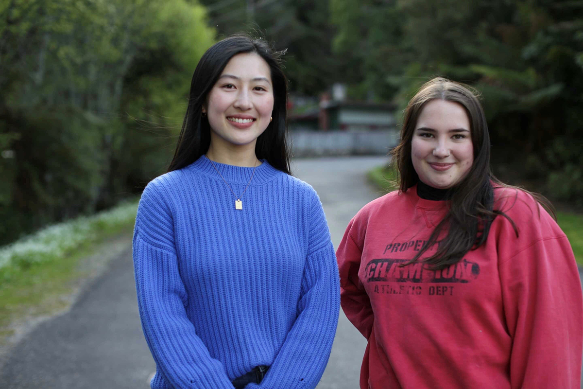 Two women standing together on a pathway, smiling at the camera.