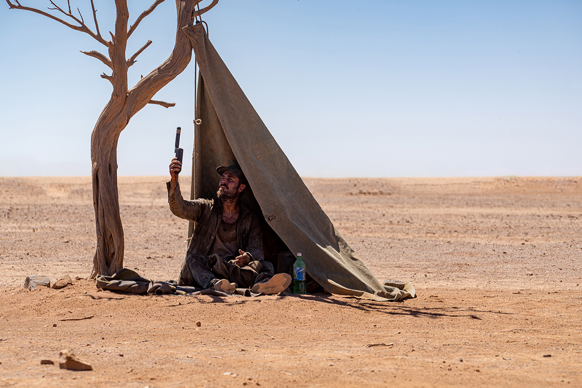 A man sits under a makeshift tent in the middle of the Australian outback.