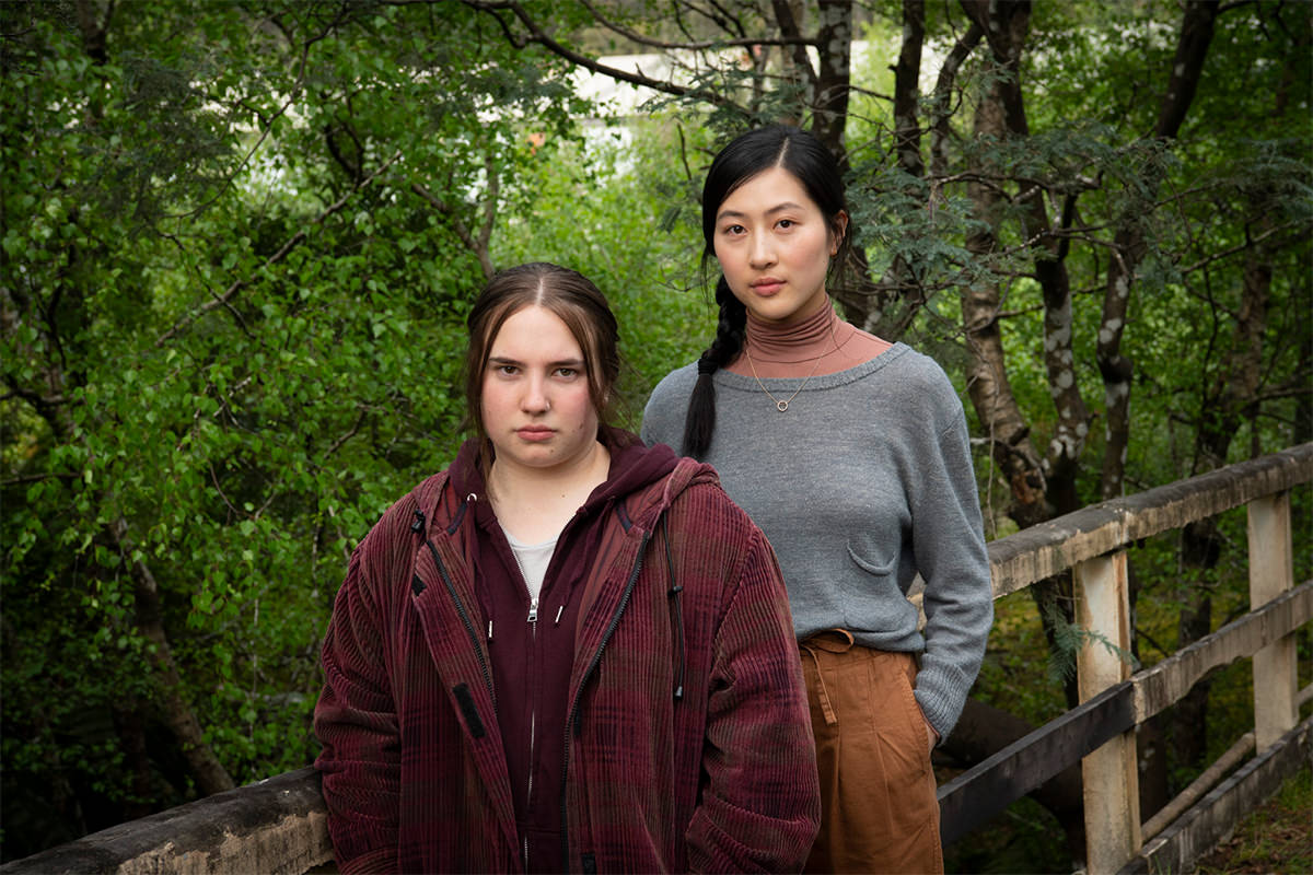 Two women standing together, lots of trees behind them.