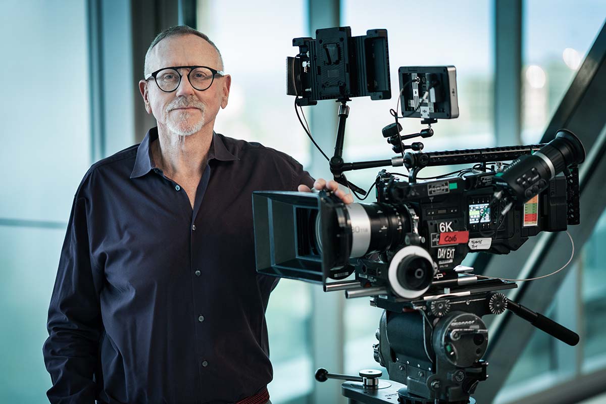 Bevan Lee stands next to a large camera.