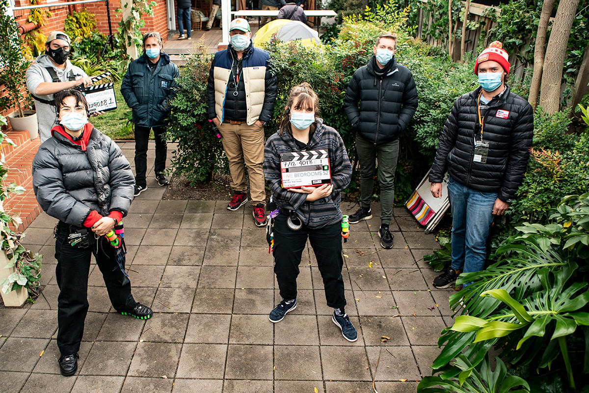 Crew gather around on the set of Five Bedrooms series 2. They are all spaced out from one another and wearing face masks.