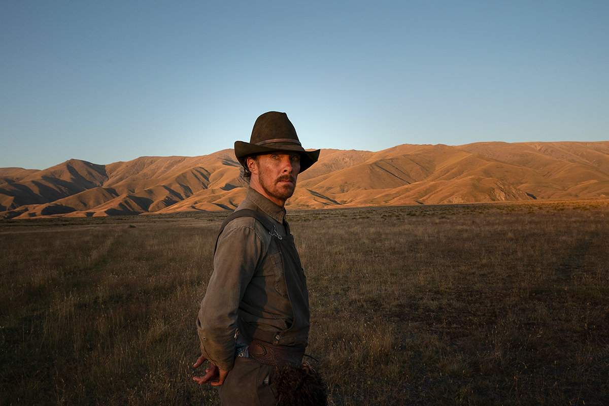 Still from The Power of The Dog. A man standing with his hand behind his back, looking towards the camera.