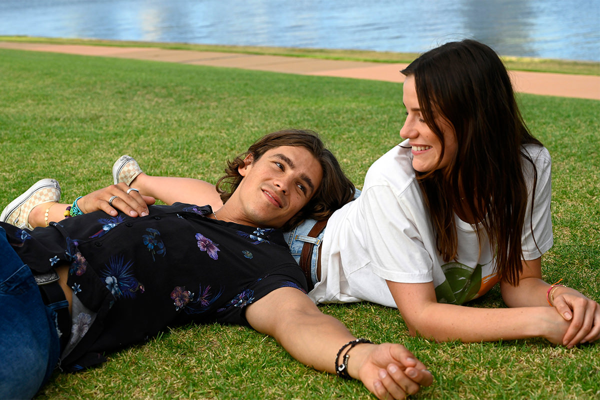 A man and a woman are lying on the grass outside, smiling.