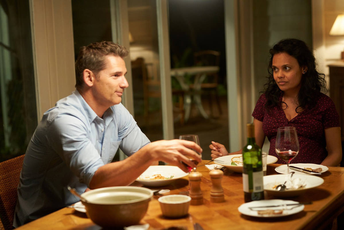 Eric Bana and Miranda Tapsell sit together at a dinner table in The Dry.