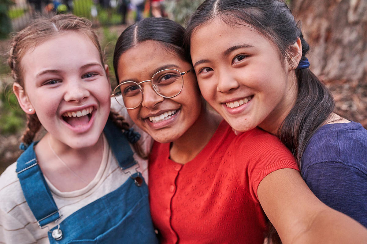 Three children take a selfie, they are smiling at the camera