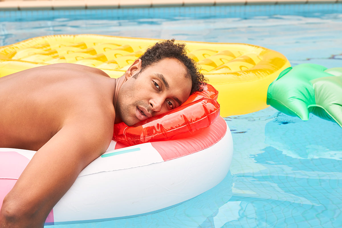 Matt Okine lying on a blow up pool toy in a pool