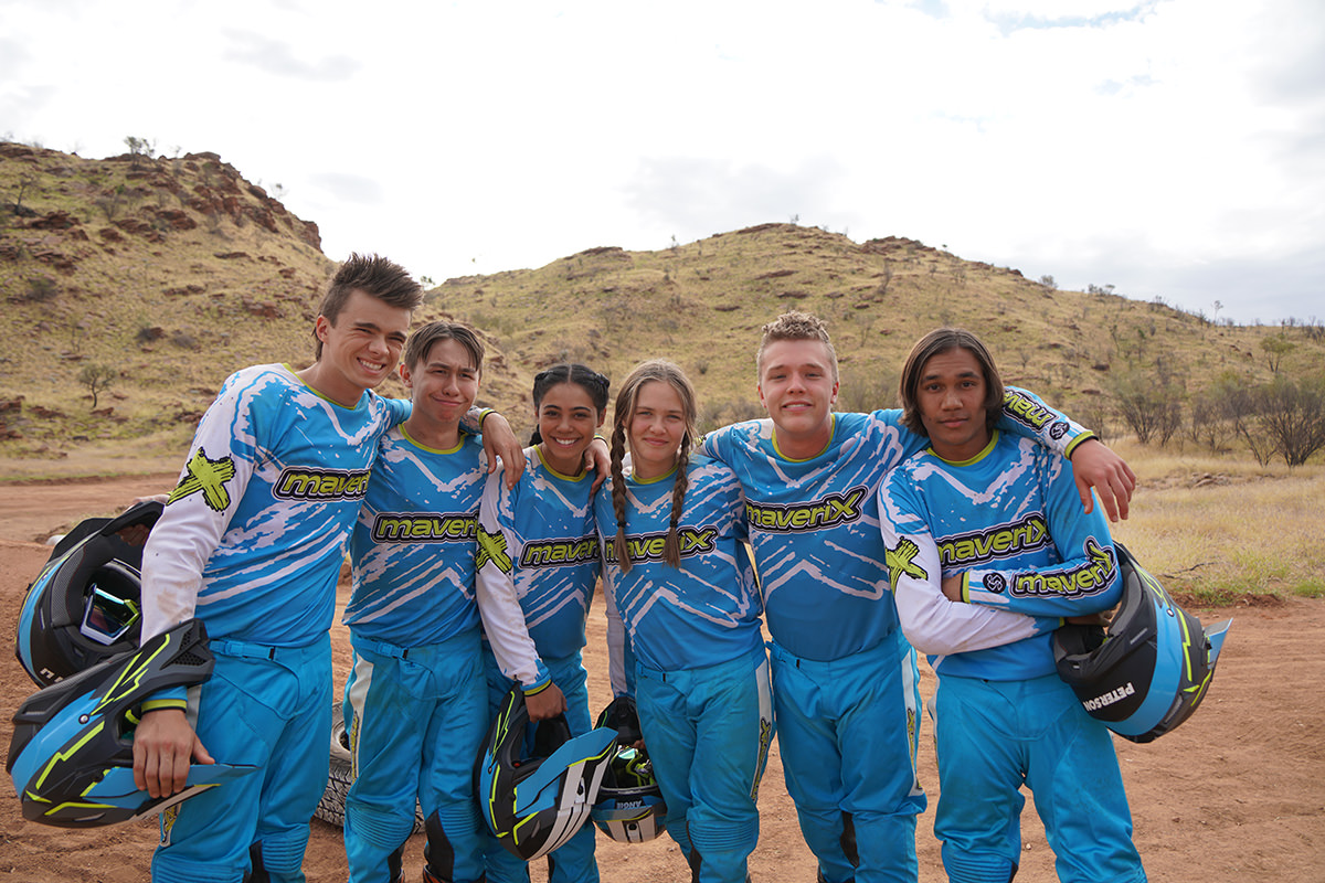 The six riders stand together, smiling.