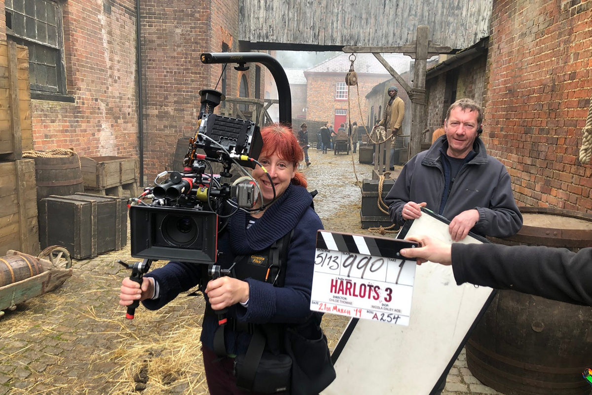 Nicola Daley holds a large camera in a narrow alley, on the set of Harlots